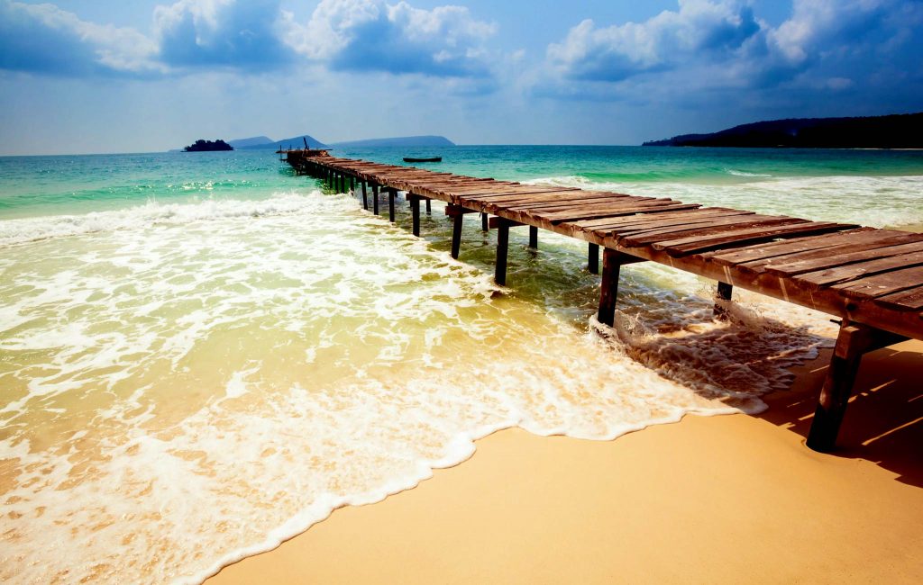 Long Set beach, Koh Rong A long white sand beach with clear blue water and a wooden bridge connecting from the shore to the sea.